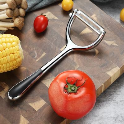 eplucheur inox gris design a coté d'une tomate planche a decouper